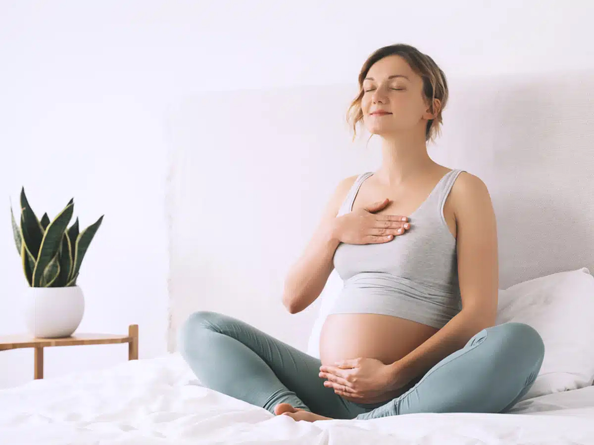 Mujer embarazada sonriendo y haciendo ejercicios de respiración para representar los beneficios de la rinoplastia antes de tener hijos.