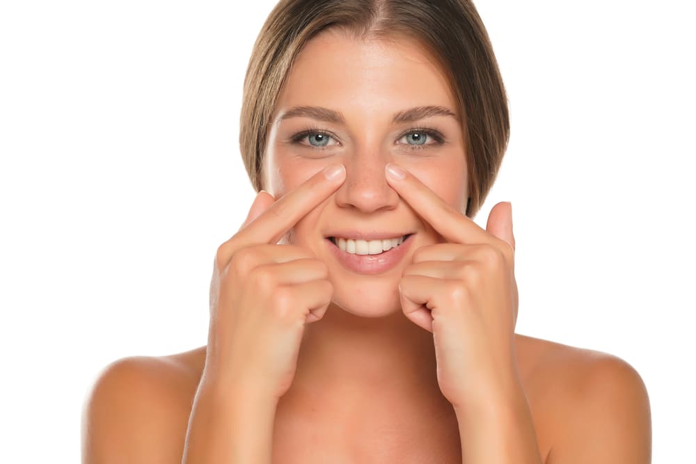 Mujer sonriendo y señalando sus fosas nasales desiguales, ilustrando el efecto de la asimetría nasal en la simetría facial.
