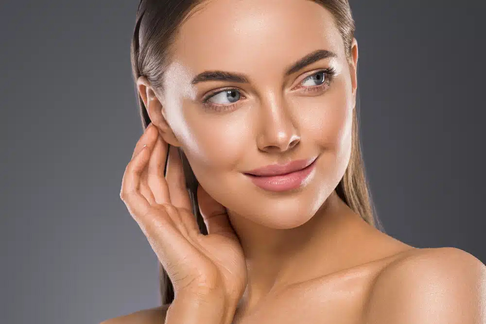 Mujer tocándose suavemente el rostro, mostrando piel saludable después de una cirugía de remodelación de las fosas nasales.