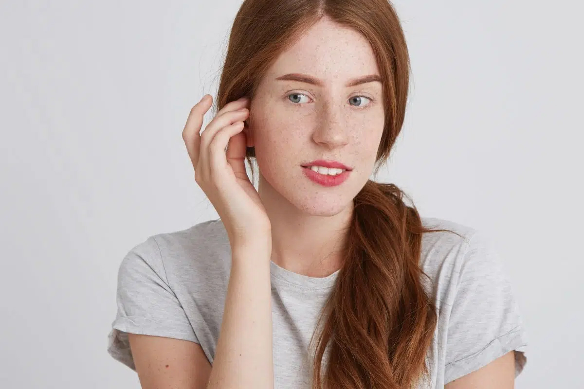 Mujer joven tocándose suavemente la oreja, demostrando cuidados después de la otoplastia para proteger el sitio quirúrgico durante la cicatrización.
