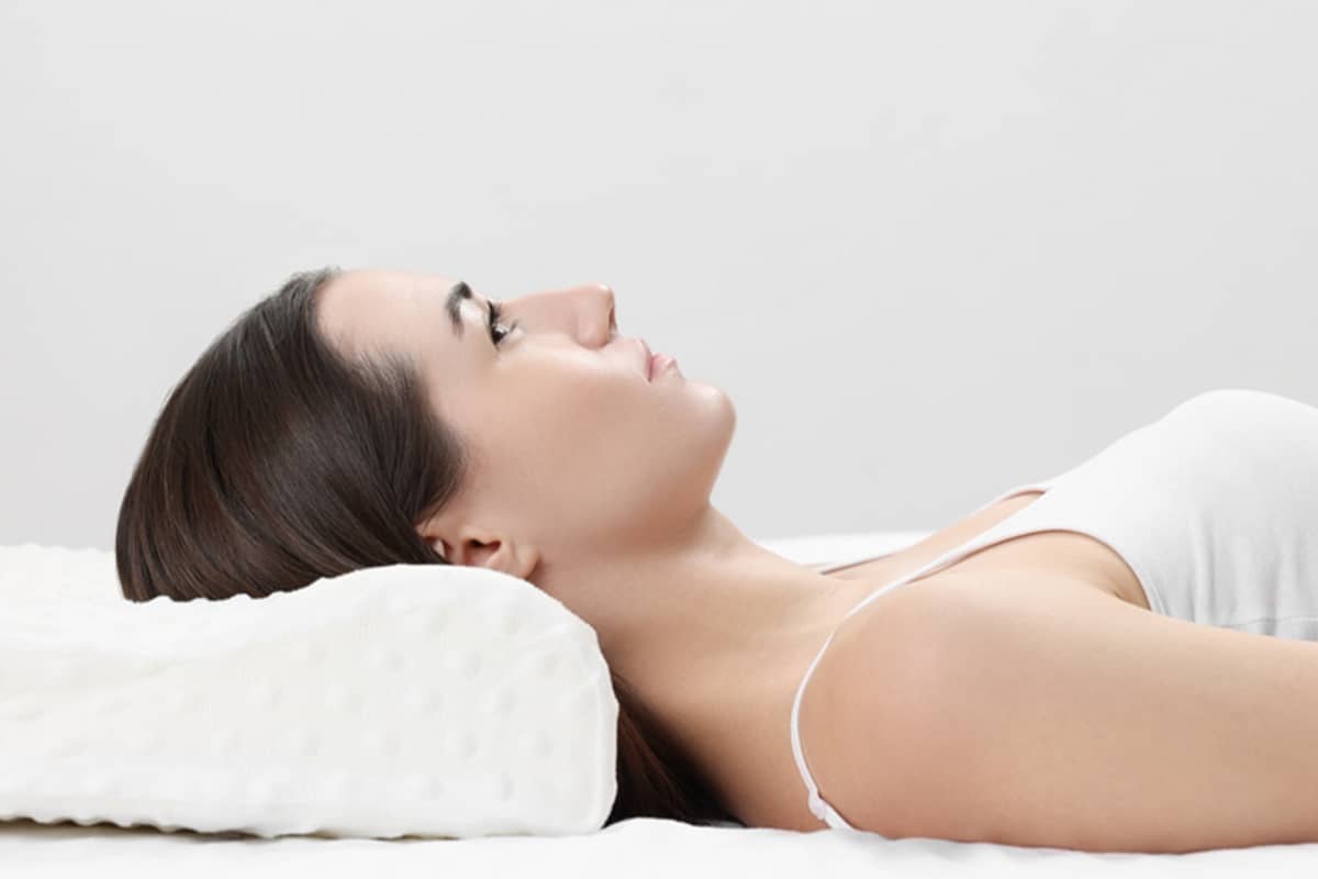 Una mujer recostada boca arriba con la cabeza elevada sobre una almohada ortopédica especializada para reducir la hinchazón durante su recuperación de lifting de plano profundo.