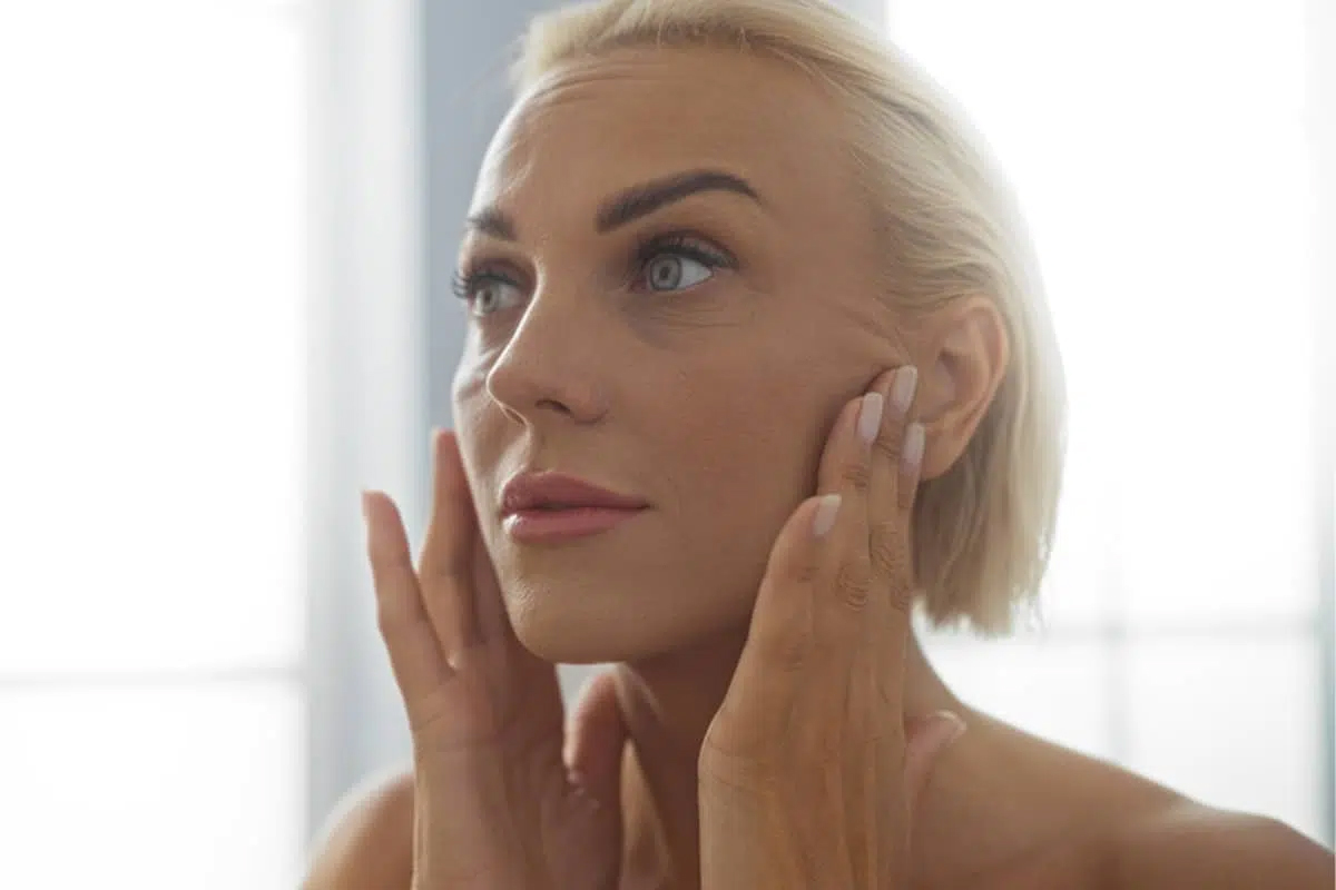 Una mujer con los ojos cerrados se toca ligeramente el rostro para monitorear el regreso gradual de la sensibilidad y la regeneración nerviosa después de un lifting facial.