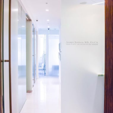 Pasillo luminoso y moderno de la clínica del Dr. Bustillo en Miami, con puerta de vidrio esmerilado y elegantes detalles de diseño.