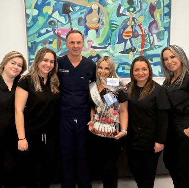 El Dr. Bustillo y su equipo sonriendo juntos, sosteniendo una canasta de regalo, con una llamativa obra de arte al fondo.