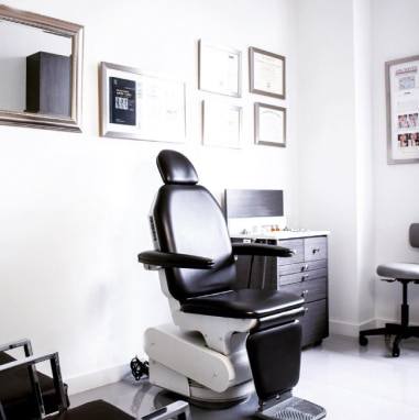 Consultorio médico moderno con un sillón de exploración negro, certificados en la pared y un ambiente acogedor.