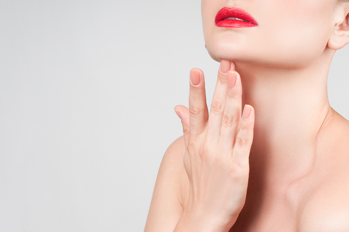 Primer plano de la elegante línea de la mandíbula de una mujer con labios rojos, destacando un cuello firme y estilizado.
