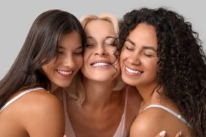 Tres mujeres sonrientes de diferentes etnias abrazándose, representando la diversidad en el lifting facial de plano profundo.