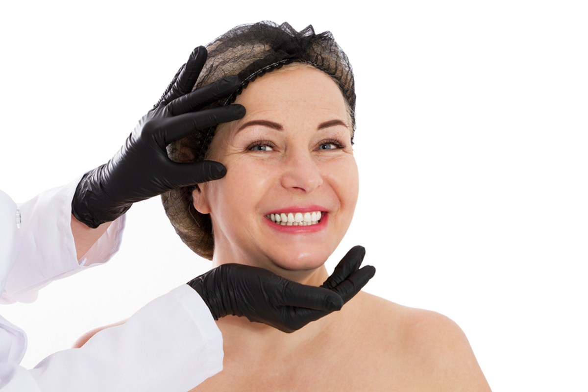 Mujer de mediana edad sonriendo mientras un médico la evalúa para rejuvenecimiento facial, lo que sugiere el momento adecuado para un lifting de plano profundo