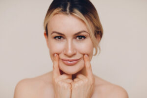Mujer presionando suavemente sus líneas de la sonrisa, ilustrando el concepto de mejora de los surcos nasogenianos y el envejecimiento facial.