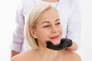 Especialista evaluando la mandíbula de una paciente sonriente para determinar el tipo de lifting facial.