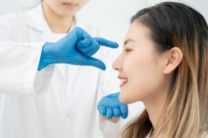 Especialista con guantes azules evaluando el perfil nasal de una paciente sonriente durante una consulta de rinoplastia.