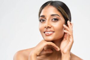 Mujer joven de ascendencia india sonriendo a la cámara, con las manos delicadamente apoyadas en su rostro y destacando sus rasgos étnicos naturales.