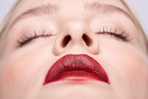 Primer plano desde un ángulo inferior del rostro de una mujer joven con los ojos cerrados y labios rojos, destacando la simetría y forma de sus fosas nasales.