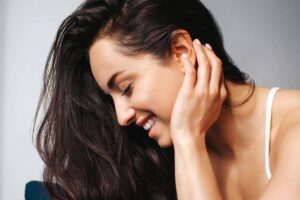 Mujer sonriendo con la cabeza inclinada y la mano cerca de la oreja, mostrando confianza tras una otoplastia.