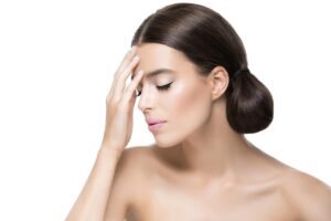 Mujer joven con los ojos cerrados tocando suavemente su frente, visualizando el proceso de recuperación facial.