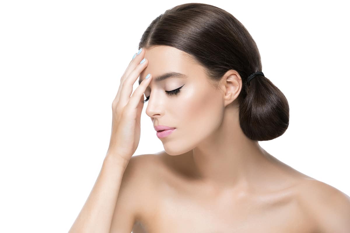 Mujer joven con los ojos cerrados tocando suavemente su frente, visualizando el proceso de recuperación facial.